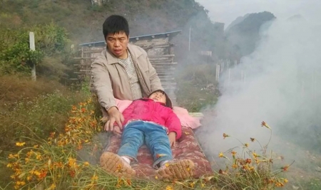 2014年11月25日，韦树福通过烧草药火熏的方式给6岁的女儿做治疗。（网络图片）