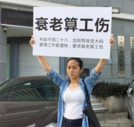 深圳一女子在南山劳动大厦举牌控诉，呼吁将“熬夜衰老列入工伤范畴”。（网络图片）
