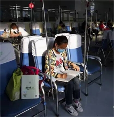 一名感冒发烧的小学生在医院输液中心边打点滴，边写作业。