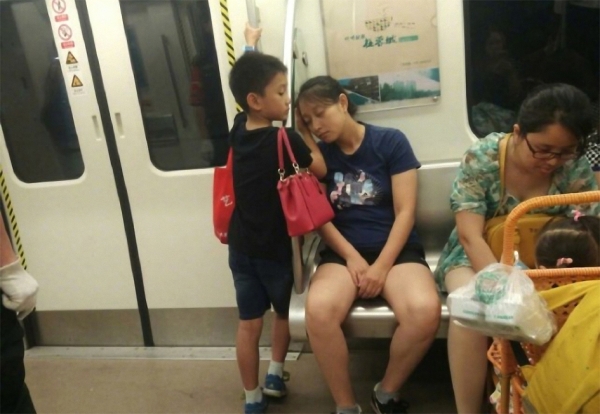 小男孩在地铁上让座、帮妈妈背包、还用手 为妈妈垫着睡觉。