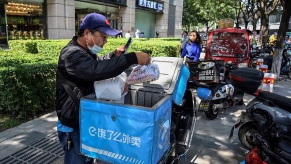  外卖人员在北京一条街道上检查食品订单，示意图。（图片来源：JADE GAO/AFP via Getty Images）