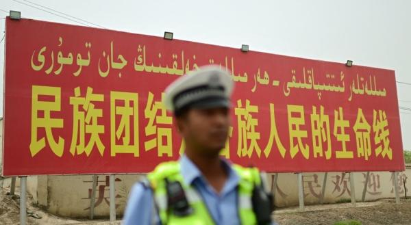 2023年7月19日的照片显示，在中国西北部新疆地区喀什地区的一条道路上，一名警察站在一个宣传广告牌前，上面写着 “ 民族团结是各族人民的生命线 ” 。（图片来源：翻拍）