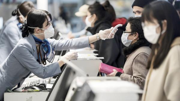 图为机场一名工作人员正在测量旅客体温。（Tomohiro Ohsumi/Getty Images）